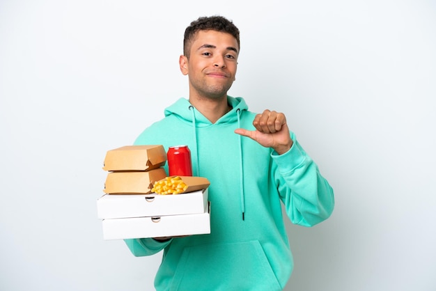 Junger Brasilianer hält Fast Food isoliert auf weißem Hintergrund stolz und selbstzufrieden