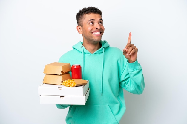 Junger Brasilianer hält Fastfood isoliert auf weißem Hintergrund und zeigt auf eine tolle Idee