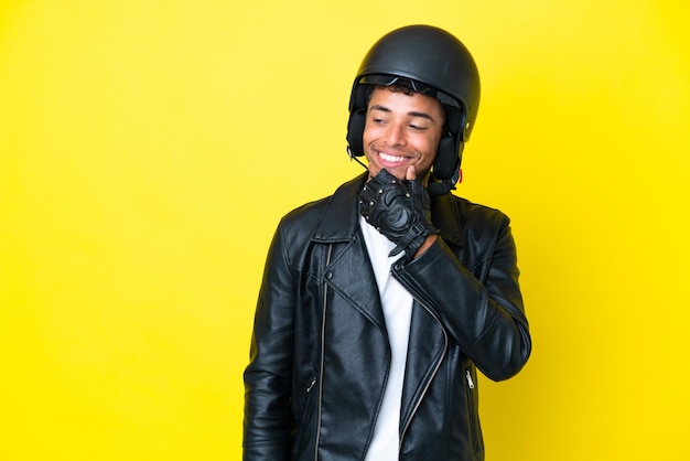 Junger Brasilianer mit Motorradhelm isoliert auf gelbem Hintergrund, der zur Seite schaut und lächelt