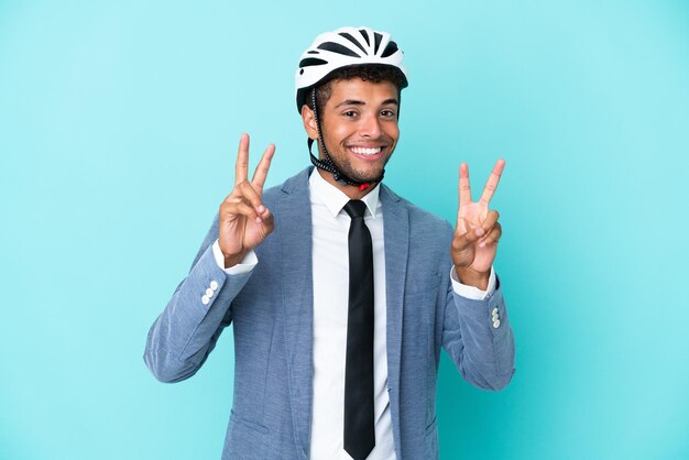 Junger brasilianischer Geschäftsmann mit Fahrradhelm isoliert auf blauem Hintergrund mit Victory-Zeichen mit beiden Händen