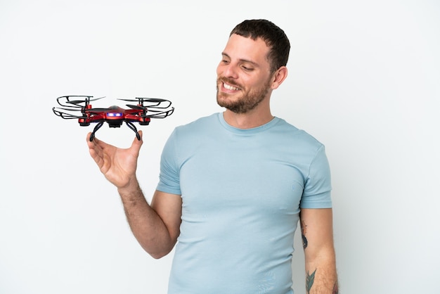 Junger brasilianischer Mann, der eine Drohne isoliert auf weißem Hintergrund hält und zur Seite schaut und lächelt