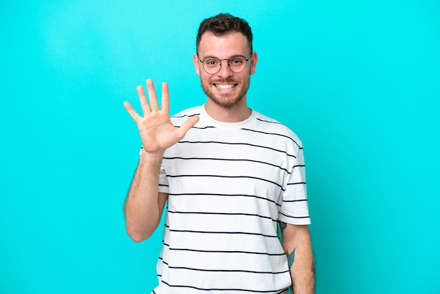 Foto junger brasilianischer mann lokalisiert auf blauem hintergrund, der fünf mit den fingern zählt