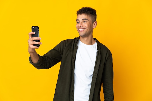 Junger brasilianischer Mann über isolierter Wand, die ein Selfie mit Handy macht