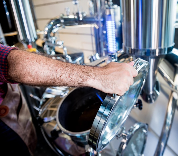 Junger Brauer in Lederschürze, der den Prozess der Biergärung in einem modernen Brauereibetrieb überwacht.