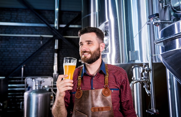 Junger Brauer mit Lederschürze testet Bier in einer modernen Brauerei