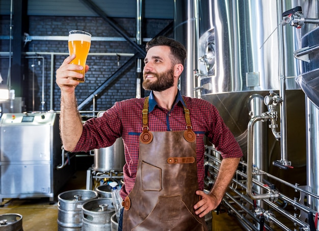 Junger Brauer mit Lederschürze testet Bier in einer modernen Brauerei