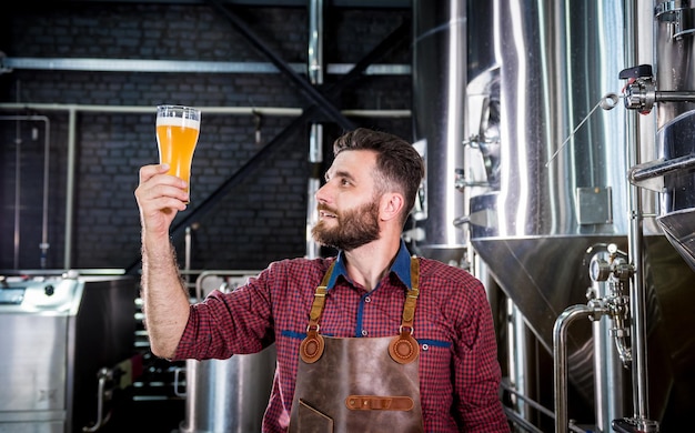 Junger Brauer mit Lederschürze testet Bier in einer modernen Brauerei