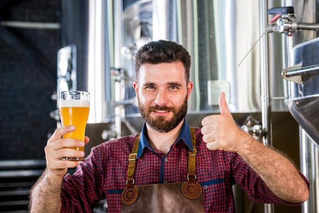 Junger Brauer mit Lederschürze testet Bier in einer modernen Brauerei