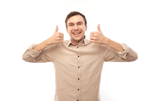 Junger brünetter Mann zeigt Hand mit erhobenem Daumen und lächelt isoliert auf weißem Hintergrund in die Kamera