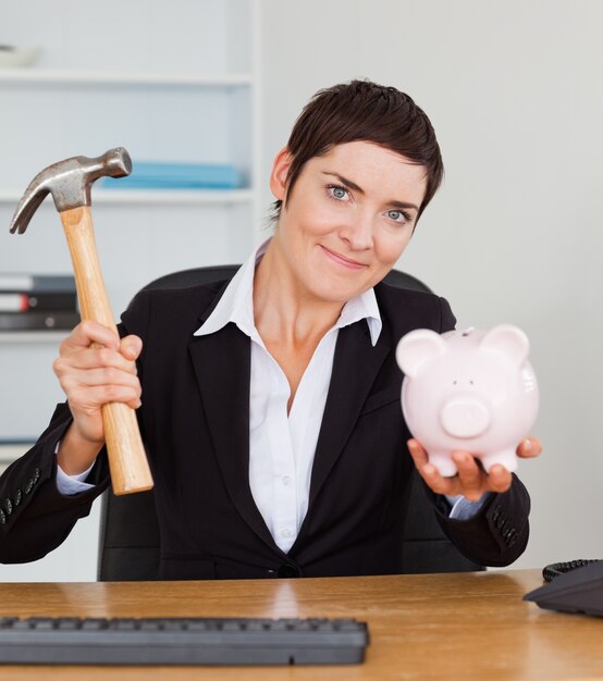 Junger Büroangestellter, der ein piggybank mit einem Hammer bricht