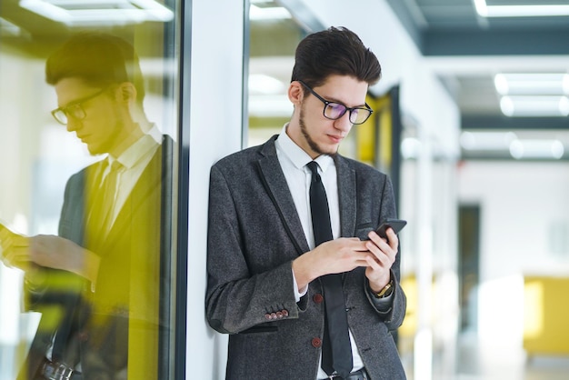 Junger Büroangestellter mit Brille und Smartphone Geschäftsmann hält Telefon in der Hand