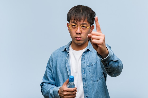 Junger chinesischer Mann, der eine Wasserflasche hält, die Nummer eins zeigt