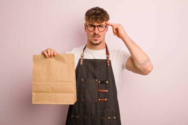 Junger cooler Mann, der sich verwirrt und verwirrt fühlt und zeigt, dass Sie ein verrückter Lieferbote und Fast Food sind