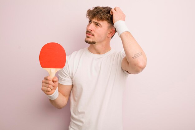 Junger cooler Mann, der sich verwirrt und verwirrt fühlt, wenn er sich das Kopf-Pingpong-Konzept kratzt