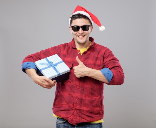 Junger cooler Mann mit Weihnachtsmann-Hut und Geschenk