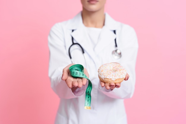 Junger Doktor hält Donut und messendes Band im Raum.