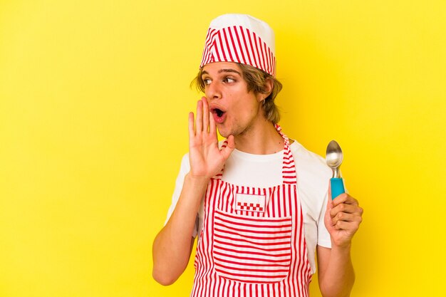 Junger Eiscreme-Mann mit Make-up, der Löffel auf gelbem Hintergrund hält, sagt eine geheime heiße Bremsnachricht und schaut beiseite