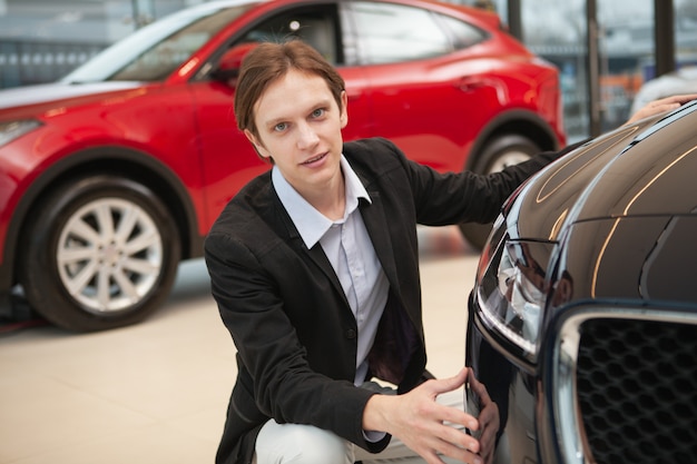 Junger eleganter Mann, der zuversichtlich schaut, während er Autos im Verkauf am Händler untersucht