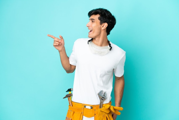 Junger Elektriker Argentinischer Mann isoliert auf blauem Hintergrund, der mit dem Finger zur Seite zeigt und ein Produkt präsentiert