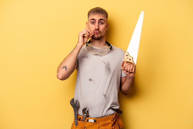 Foto junger elektriker, kaukasischer mann isoliert auf gelbem hintergrund mit fingern auf den lippen, die ein geheimnis bewahren.