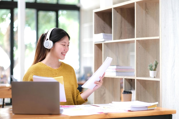 Junger Erwachsener, glücklich lächelnde hispanische asiatische Studentin mit Kopfhörern, die über Online-Chat-Meetings mit Laptops auf dem Universitätscampus oder im virtuellen Büro spricht College-Studentin, die aus der Ferne lernt