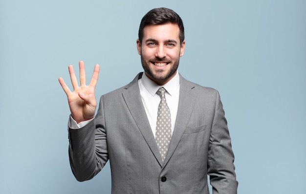 Junger erwachsener, gutaussehender Geschäftsmann, der lächelt und freundlich aussieht, Nummer vier oder vier mit der Hand nach vorne zeigt, herunterzählt