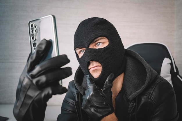 Junger Erwachsener in schwarzer Kleidung mit verstecktem Gesicht Illintended Betrüger verwendet Handy Betrüger ruft Scam Handy-Schläger an Hacker entführt per Telefon Handy-Konto-Betrug