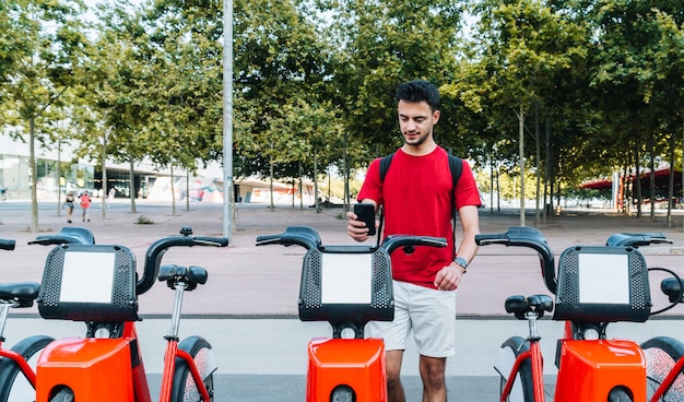 Junger erwachsener kaukasischer Student, der mit seinem Smartphone ein Leihfahrrad bucht