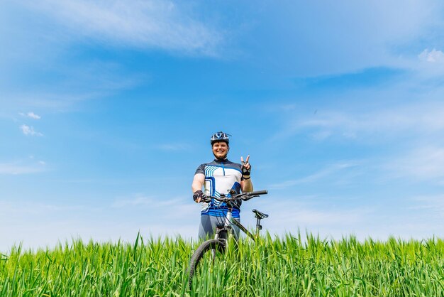 Junger erwachsener lächelnder mann, der mit fahrrad in grüner gerste fi steht