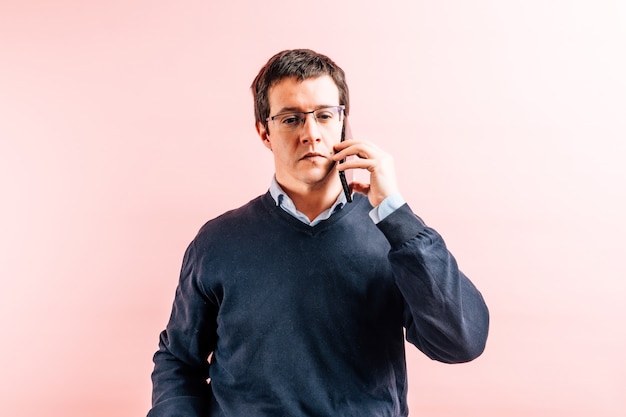 Junger erwachsener Mann fünfunddreißig Jahre alt in blauem Hemd mit V-Ausschnitt und Pullover mit rosa Hintergrund ernsthafte Gespräche auf dem Smartphone