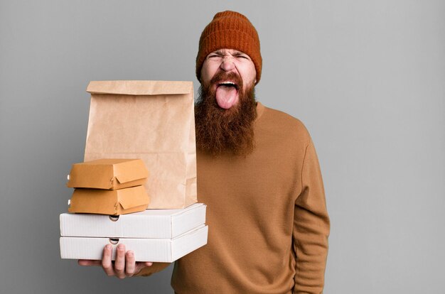 Junger erwachsener rothaariger bärtiger cooler Mann mit einer Papiertüte mit Essen zum Mitnehmen