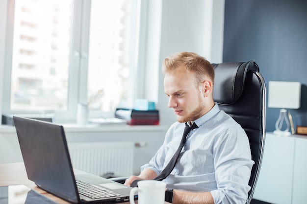 junger europäischer Geschäftsmann arbeitet an einem Laptop in einem modernen hellen Büro