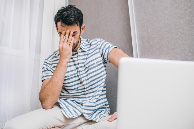 Junger europäischer gestresster Mann, der erschöpft aussieht und sein Gesicht mit der Hand bedeckt, während er zu Hause auf dem Boden sitzt Gefühl von Enttäuschung und Frustration Geschäfts- und Lifestyle-Konzept der Menschen