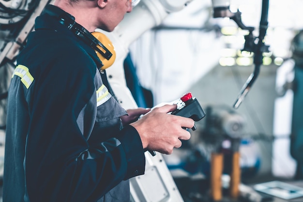 Junger Fabrikarbeiter, der mit einem geschickten Roboterarm arbeitet