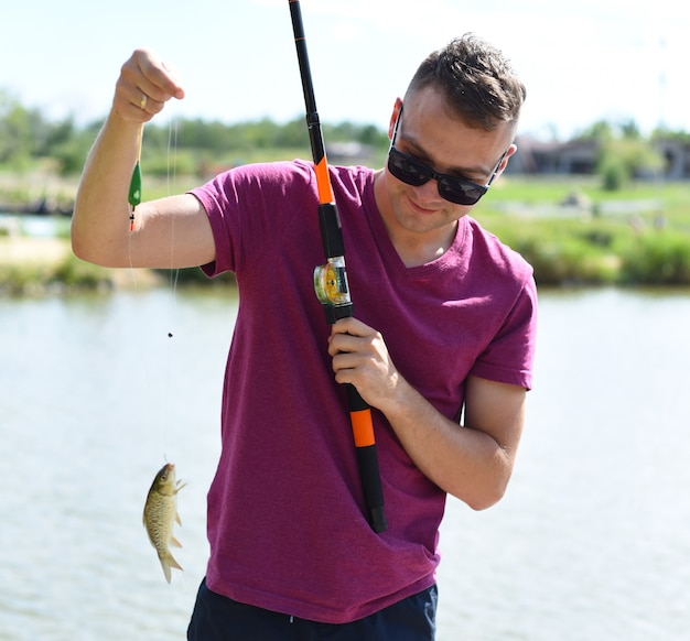 Junger Fischer, der Karausche auf Angelrute gegen einen Teich hält