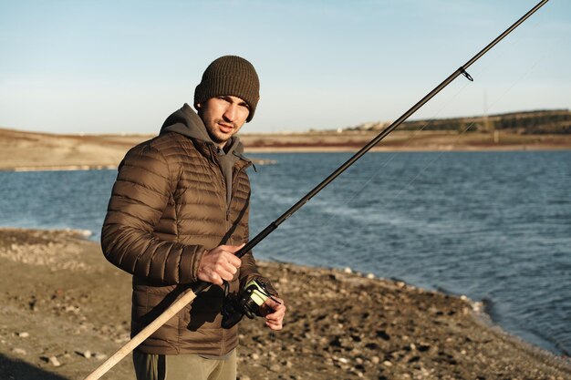 Junger Fischer, der mit Angelrute am Ufer des Sees steht