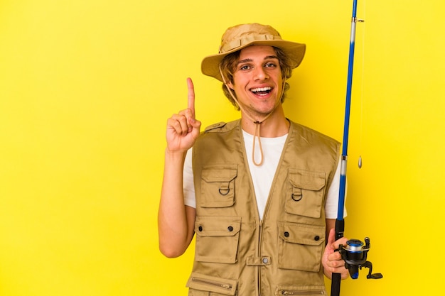 Junger Fischer mit Make-up-Haltestange auf gelbem Hintergrund isoliert, die Nummer eins mit dem Finger zeigt.