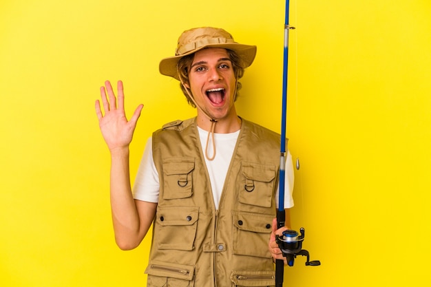 Junger Fischer mit Make-up-Haltestange isoliert auf gelbem Hintergrund lächelnd fröhlich mit Nummer fünf mit den Fingern.