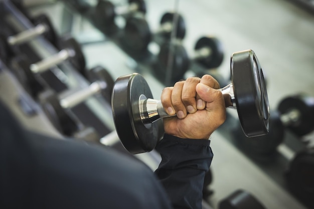 Junger Fitness-Mann mit Dummkopf im Fitnessstudio. Guy Krafttraining mit Sportbekleidung. Asiatischer Mann trainiert Indoor-Fitnessstudio mit Hantel. Bodybuilder gute Gesundheit