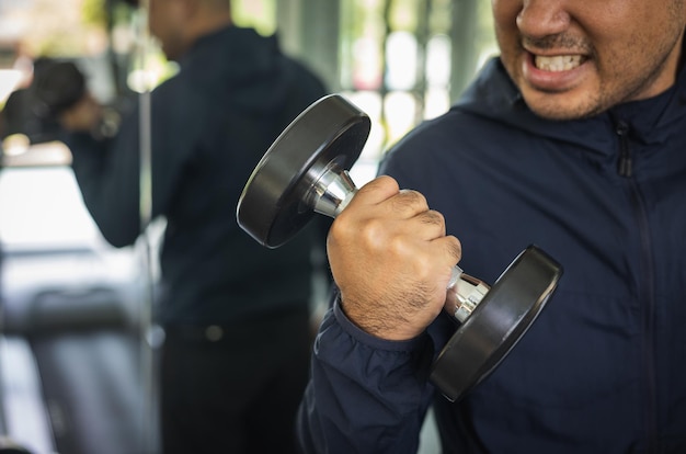 Foto junger fitness-mann mit dummkopf im fitnessstudio. guy krafttraining mit sportbekleidung. asiatischer mann trainiert indoor-fitnessstudio mit hantel. bodybuilder gute gesundheit