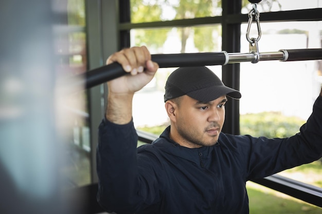 Junger Fitness-Mann zieht die Maschinenstange im Fitnessstudio hoch. Guy Krafttraining mit Sportbekleidung. Asiatischer Mann trainiert Indoor-Fitnessstudio. Bodybuilder gute Gesundheit