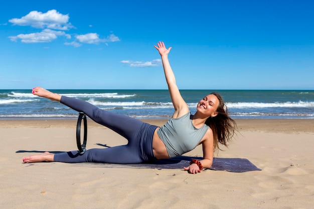 Junger Fitnesstrainer mit einem Pilates-Ring in der Nähe des Meeres weibliches Fitness-Yoga-Routine-Konzept