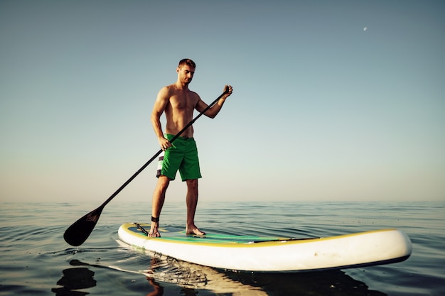 Junger fitter Mann auf Paddle-Board, der auf dem See schwimmt