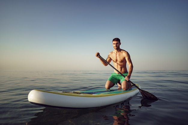 Junger fitter Mann auf Paddle-Board, der auf dem See schwimmt