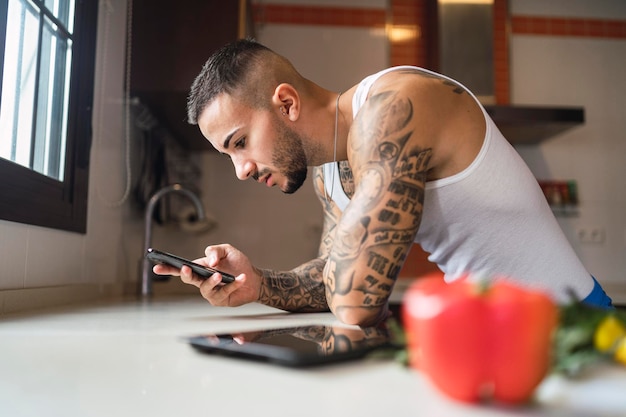 Junger fitter Mann, der sein Smartphone benutzt, während er in der Küche gesundes Essen kocht