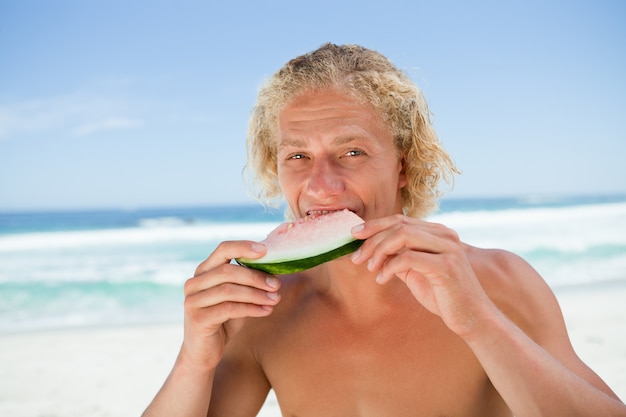 Junger Fleisch fressender ein Stück Wassermelone vor dem Meer