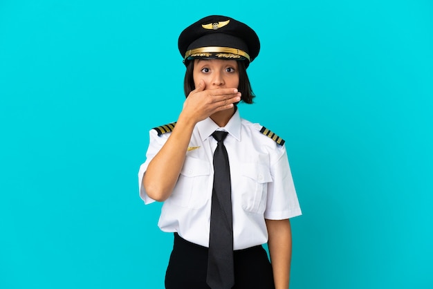 Junger Flugzeugpilot über isoliertem blauem Hintergrund, der den Mund mit der Hand bedeckt
