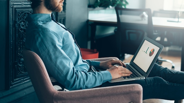 Junger fokussierter gesichtsloser Mann, der an Laptop arbeitet