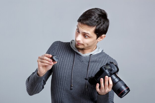 Junger Fotograf im Hemd richtet die Kamera ein. Kerl lernt auf grauem Hintergrund zu fotografieren