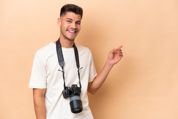 Junger Fotograf kaukasischer Mann isoliert auf beigem Hintergrund, der mit dem Finger zur Seite zeigt